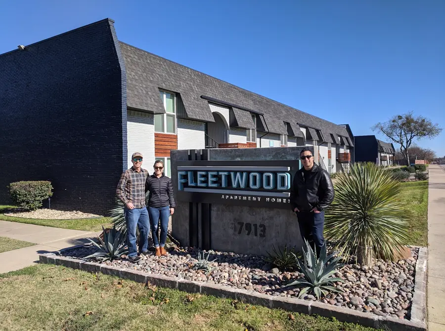 Three people standing in front of the Fleetwood Apartment Homes sign at an apartment community